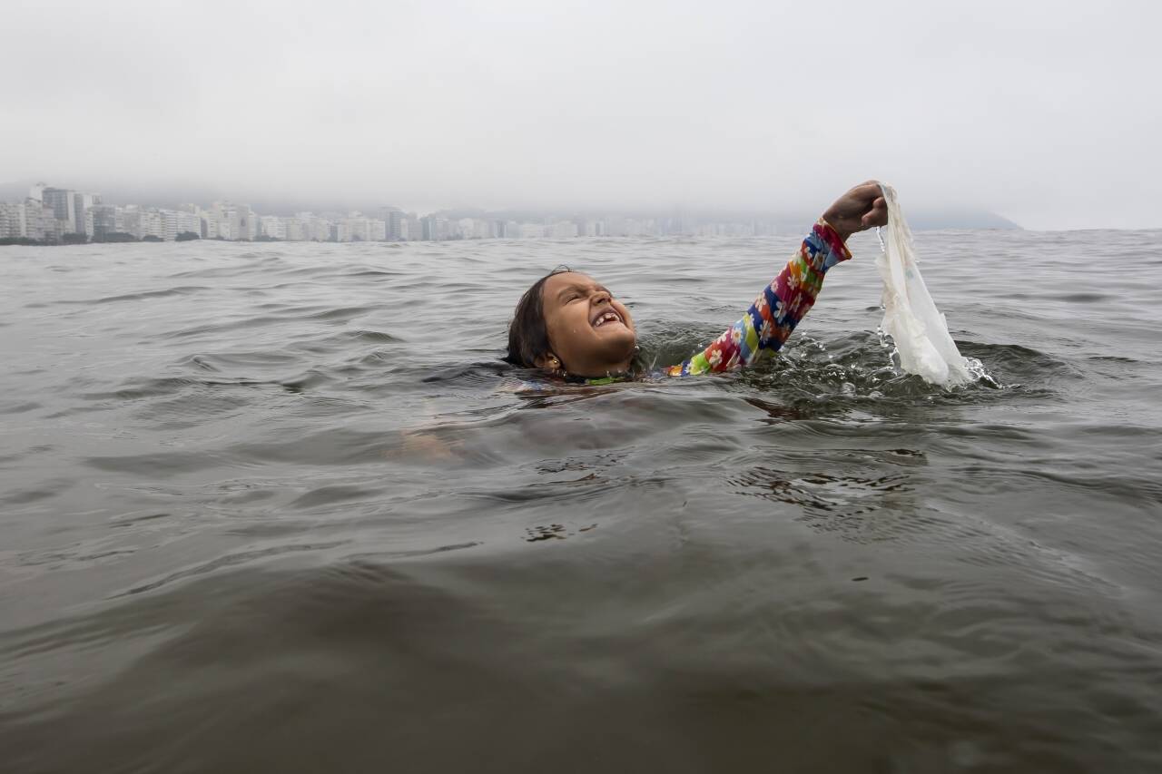 En jente henter i land en plastpose som ligger og flyter i havet i nærheten av Copacabana-stranden i Rio de Janeiro i Brasil. Norge er blant landene som jobber for å få til en internasjonal avtale mot plastforurensing. Foto: Bruna Prado / AP / NTB