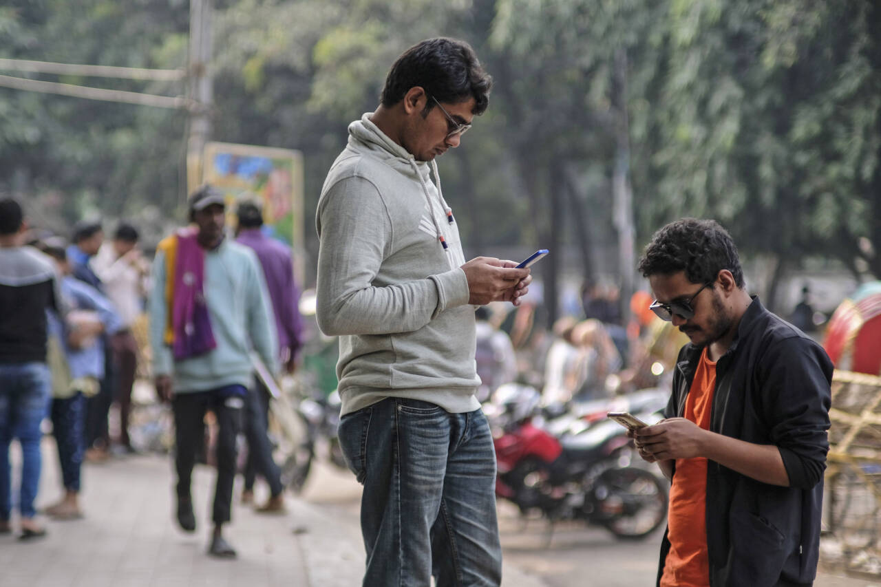 Studenter i Bangladesh med blikket rettet mot mobilen ved et universitetsområde i hovedstaden Dhaka. En kvinnelige politiker i Bangladesh dukket nylig opp i bikini i en forfalsket video. Foto: Mahmud Hossain Opu / AP / NTB